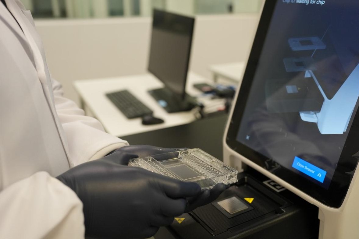 A scientist in gloves loading a chip into the instrument drawer in the Arcadia laboratory